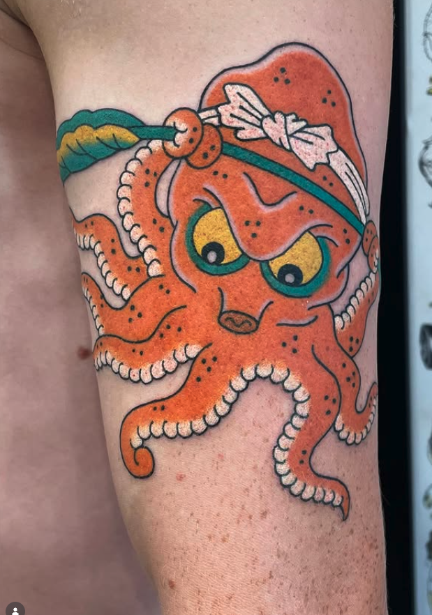Tattoo of an orange octopus with yellow eyes and a white bandana on its head, holding a green leafy plant.