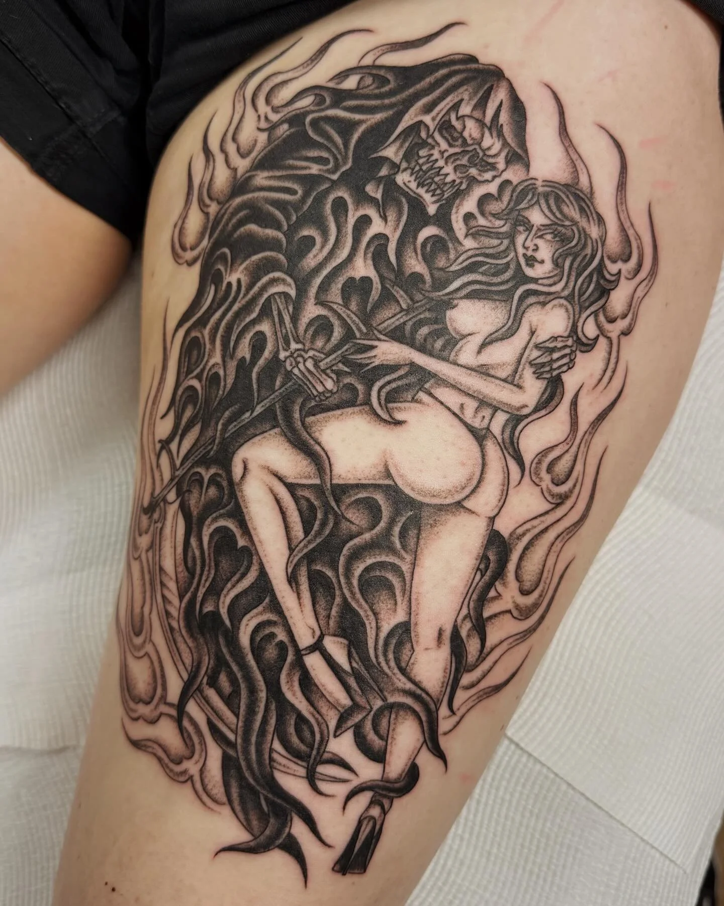 Black tattoo of a woman with long hair holding a sword, standing near a large snarling creature with horns and sharp teeth, surrounded by wavy flames or smoke.