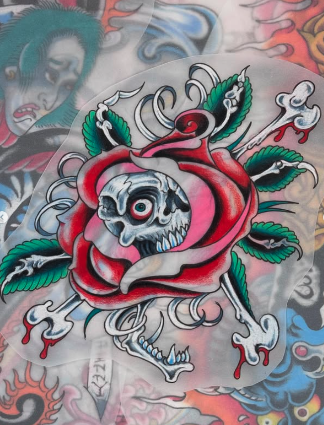Tattoo art of a skull with a single eye, surrounded by a red rose and green leaves, with dripping elements.