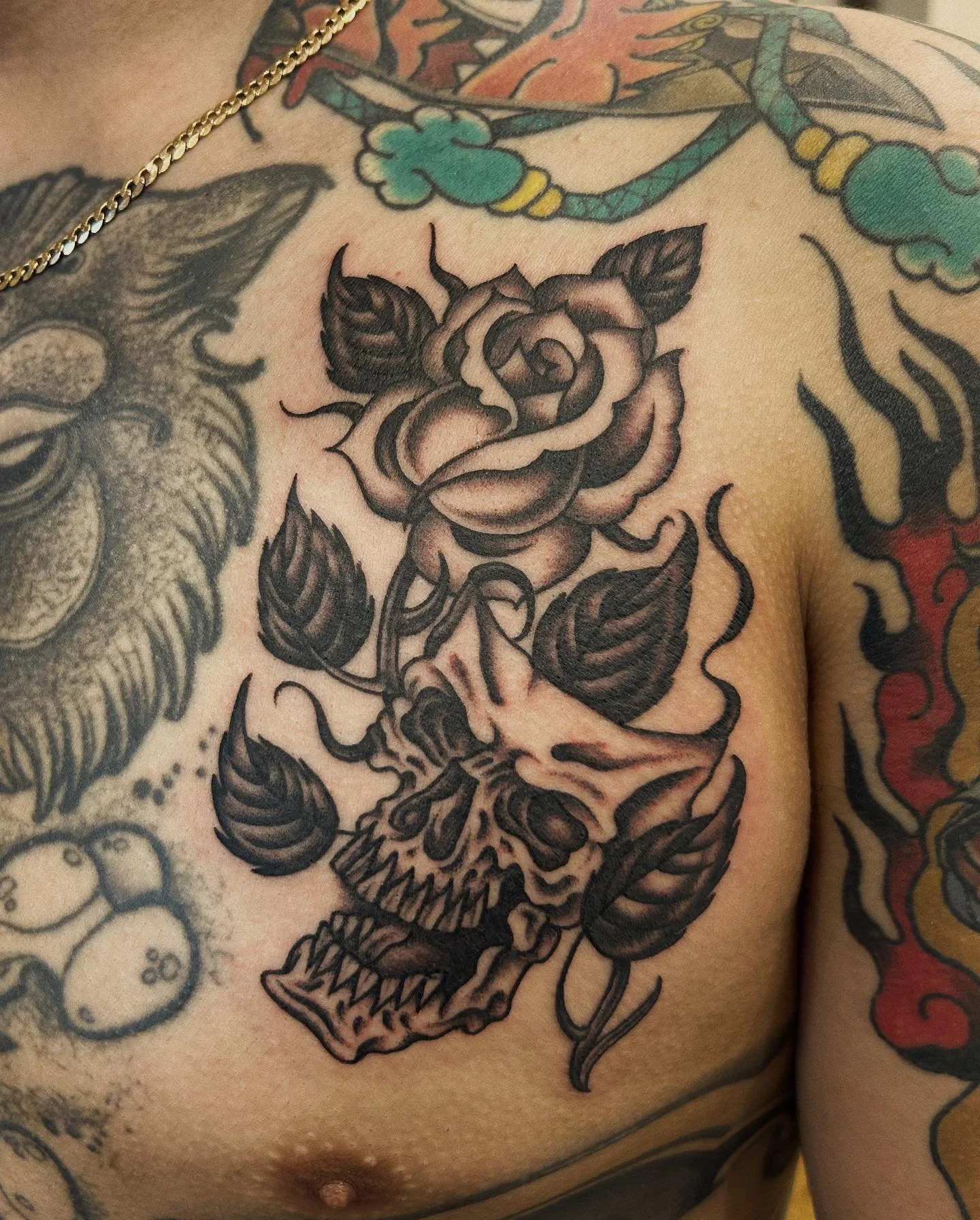 A tattoo of a human skull with a blooming rose on top, surrounded by dark leaves.