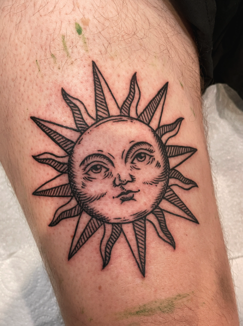 Tattoo of a sun with a human face on a person's thigh