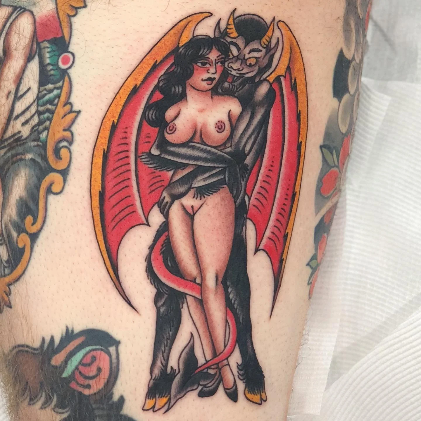 Tattoo of a woman with black hair and a succubus with horns behind her, both surrounded by a decorative border.