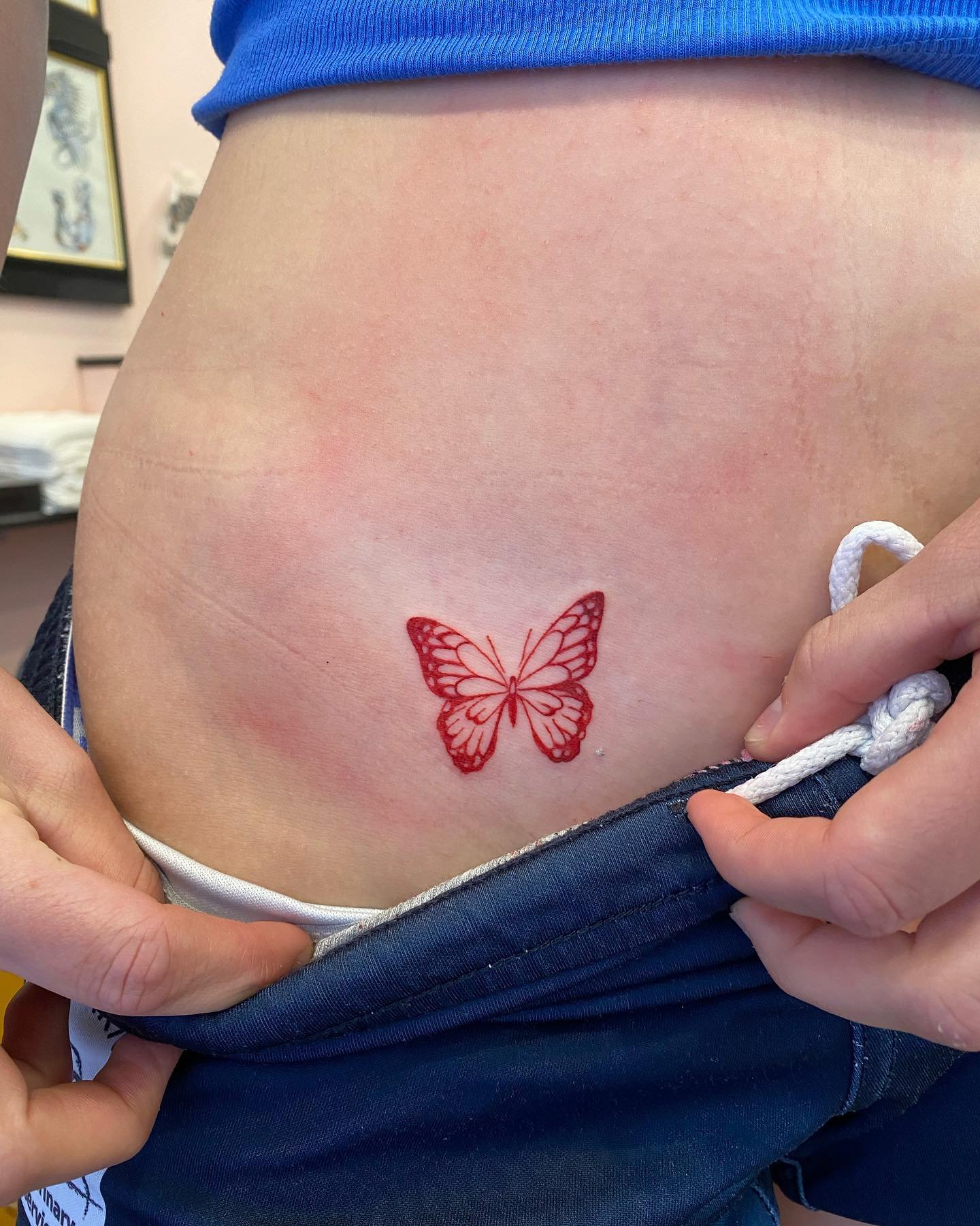 A person's side waist with a fresh red butterfly tattoo.