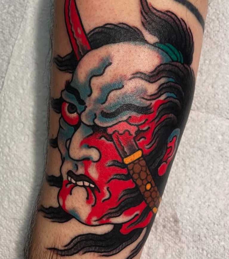 Tattoo of a woman's face with smoke and red paint, holding a lit cigarette.