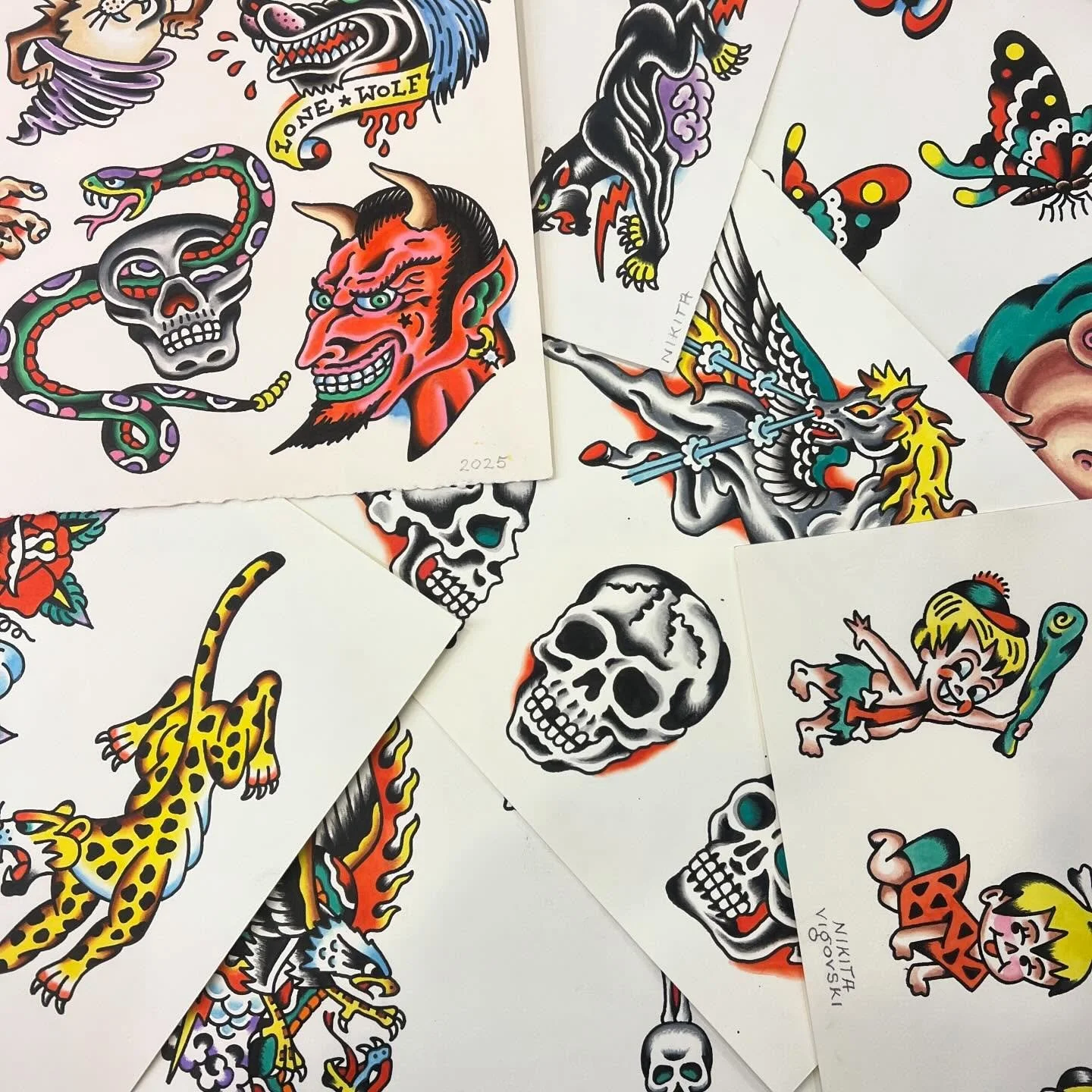 A collection of colorful tattoo-style illustrations on white paper sheets, featuring various designs such as skulls, a devil face, a snake, a girl with a bat, a dragon, a leopard, a butterfly, and a wolf, with some signatures and dates visible.