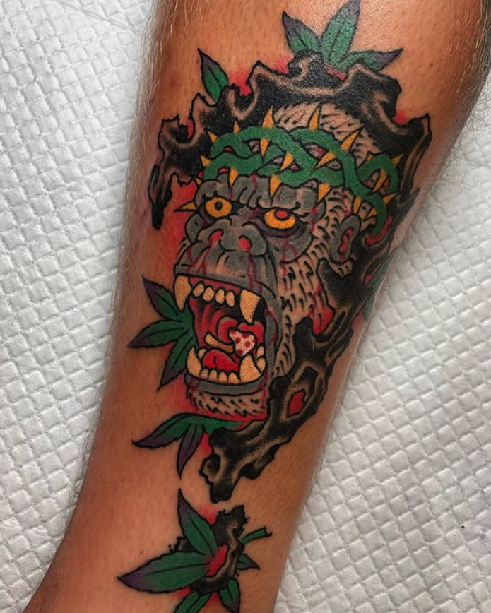 Tattoo of a roaring gorilla's face with green leaves and brown branches.