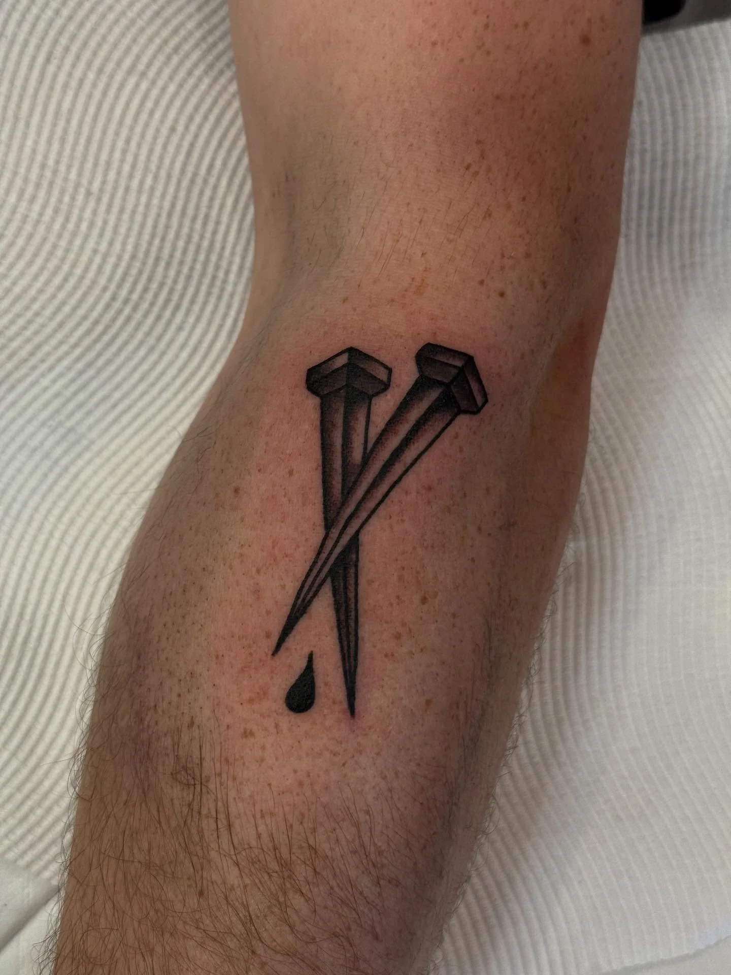 Tattoo of two black nails with a small black droplet below, on a person's arm.