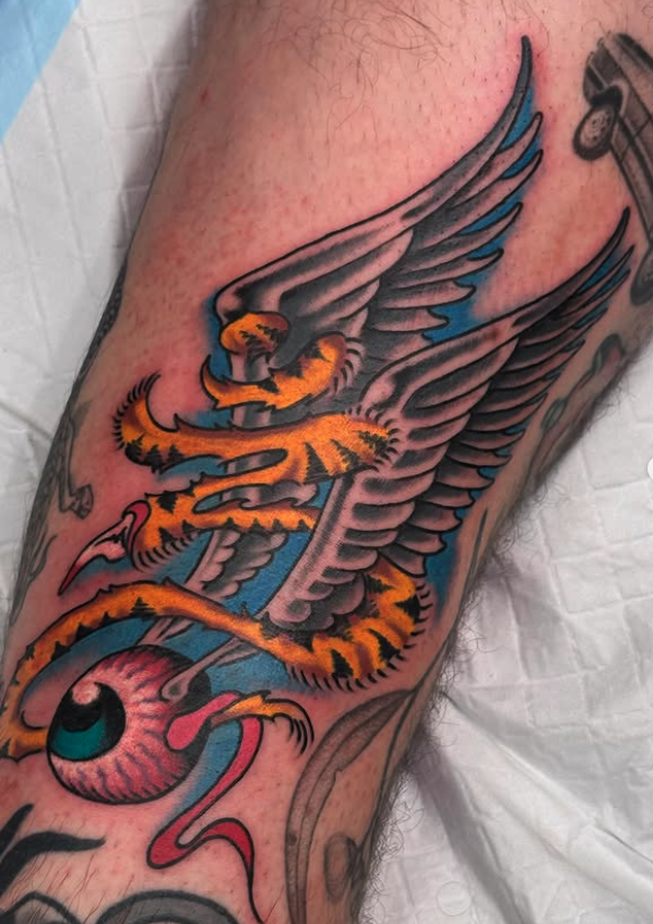 Tattoo of a winged tiger intertwined with a pink eyeball on a person's arm.
