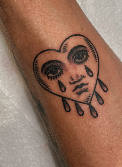 Tattoo of a crying heart with a woman's face and tears under her eyes.