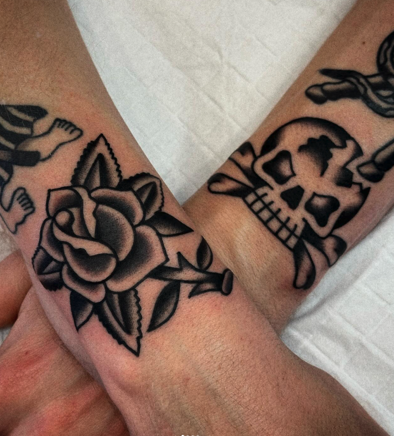 Tattoo of a rose on one person's wrist and a skull with a crossbones on the other wrist.