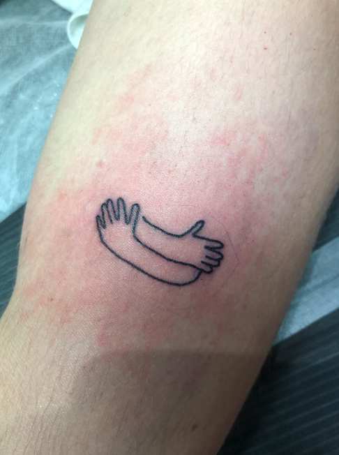Tattoo of two arms hugging each other on a person's skin.