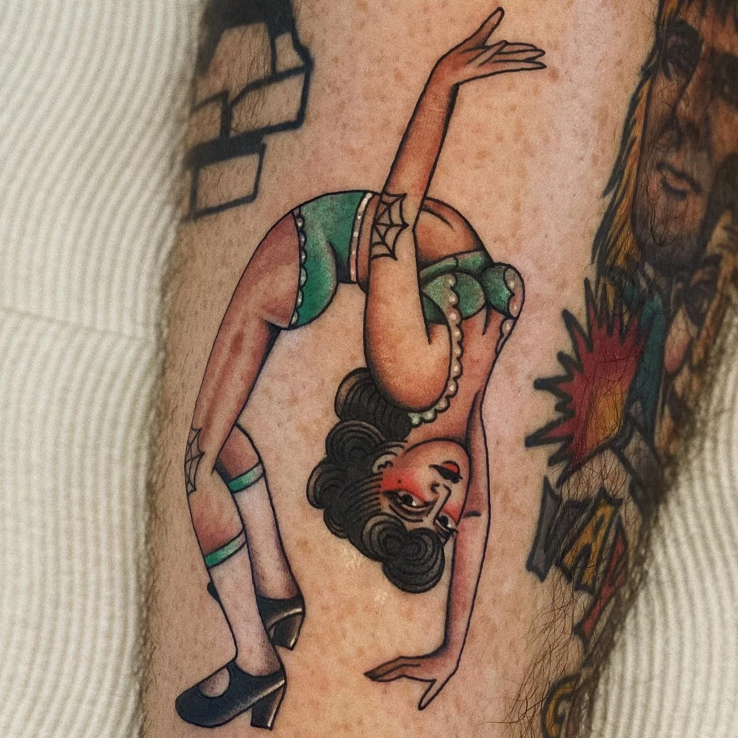 A traditional tattoo of a pin-up girl in a vintage style, with dark hair, red lipstick, green shorts, and playing with her hair.