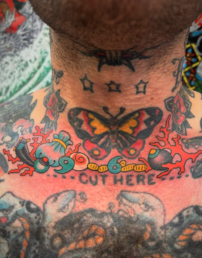 Tattooed neck and chest with colorful designs including a butterfly, cartoon bombs, and the phrase 'cut here'.