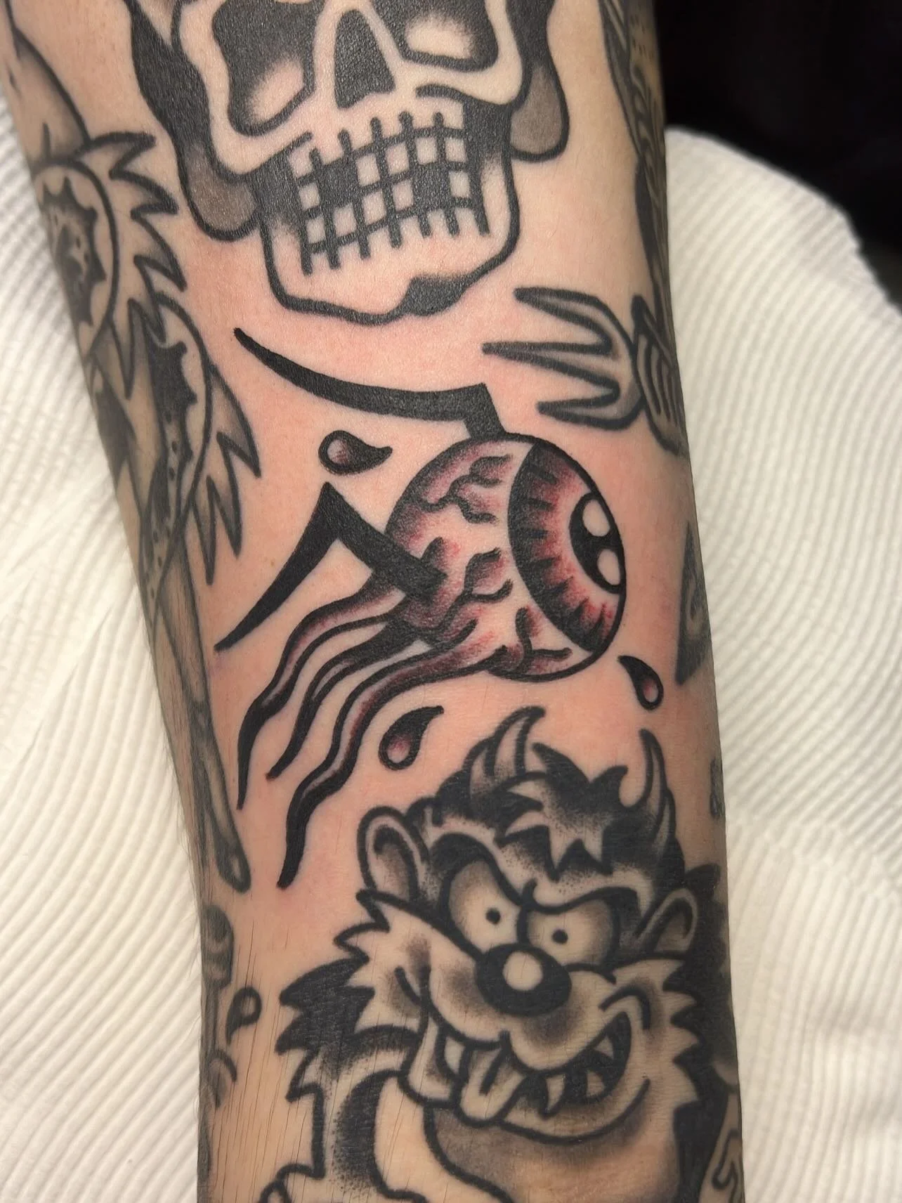 Close-up of a tattoo sleeve with a skull, a jellyfish, and a cartoonish character, all in black ink with some shading.