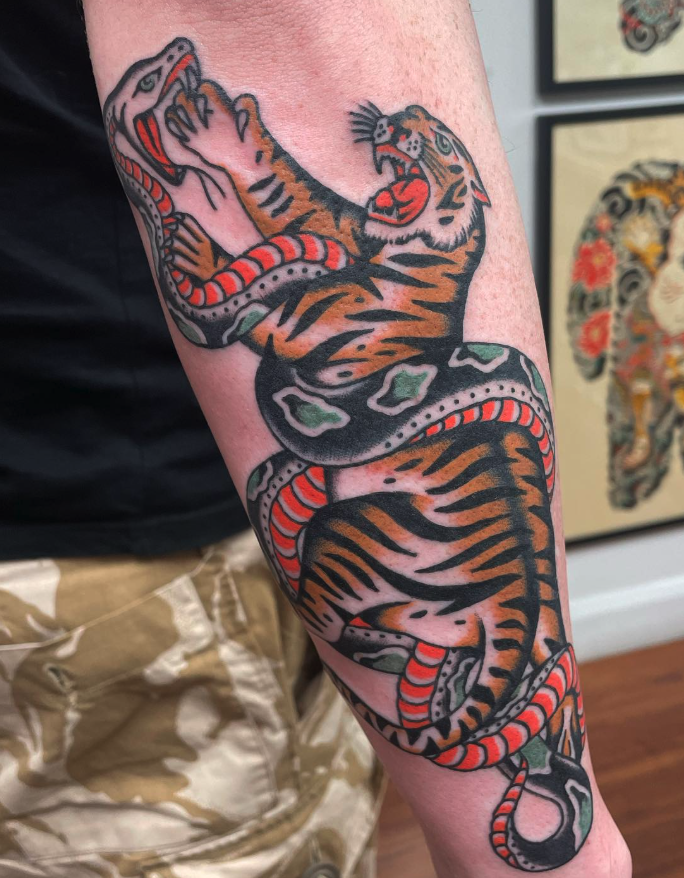 Tattoo of a tiger and snake intertwined on a person's arm.