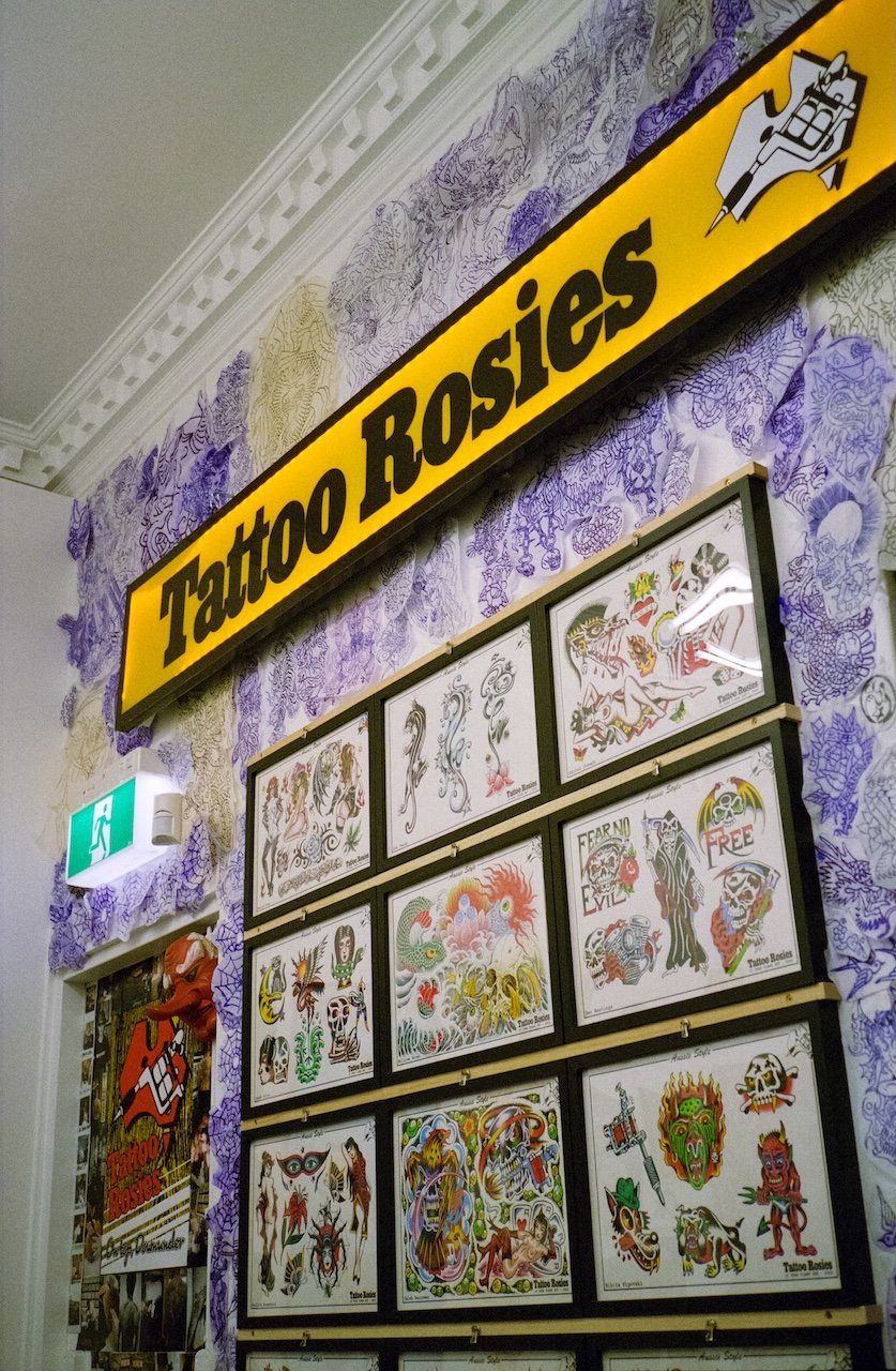 Display of various colorful tattoo flash designs on a wall for Tattoo Rosies tattoo studio.