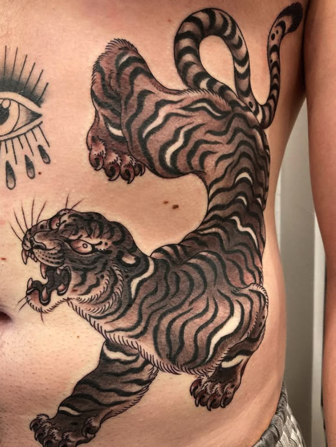 Tattoo of a roaring tiger with black and white striped fur on a person's torso.
