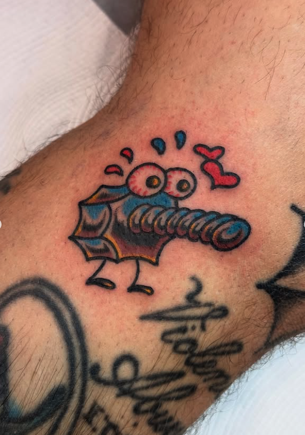 A colorful tattoo of a cartoon-style knife with eyes and a surprised expression, with red hearts and blue drops above it on a person's arm.