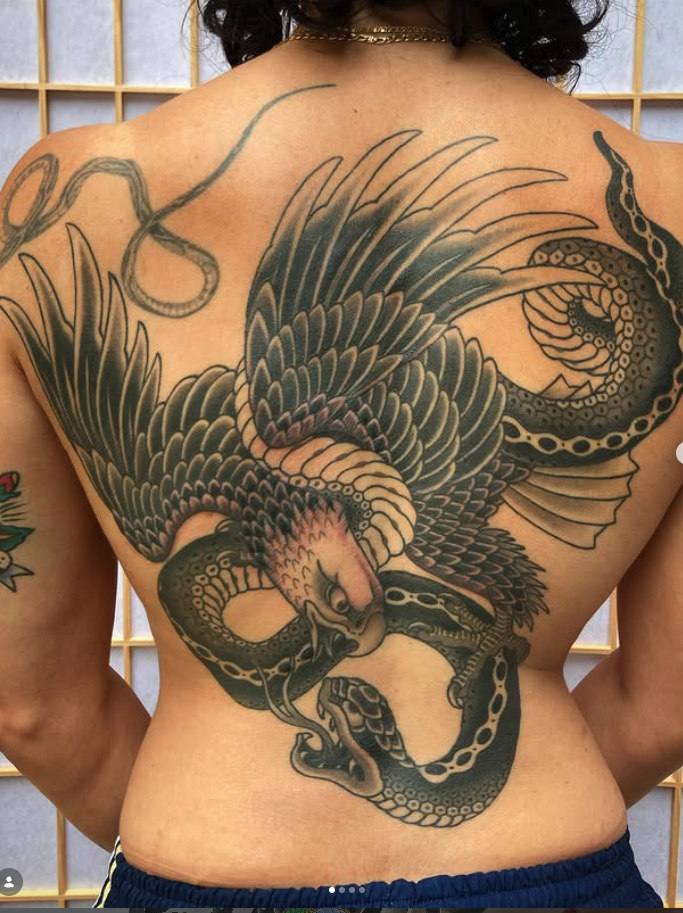 Detailed black and gray tattoo of a fierce dragon and snake intertwined across a person's back.