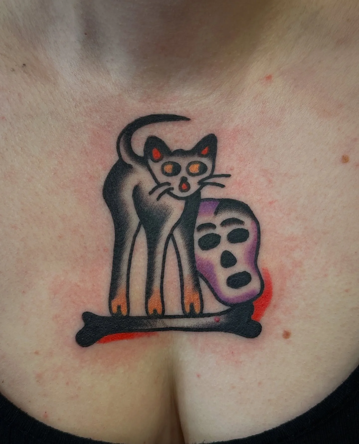 Tattoo of a cartoonish black cat with orange eyes, next to a white skull with black eyes and purple shading, on the neck.