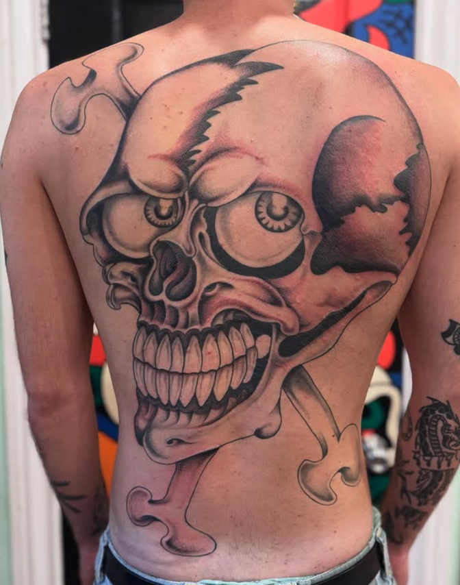 Large tattoo of a skull with exaggerated teeth and hollow eye sockets, with smoke or vapor curling around it, covering the person's chest