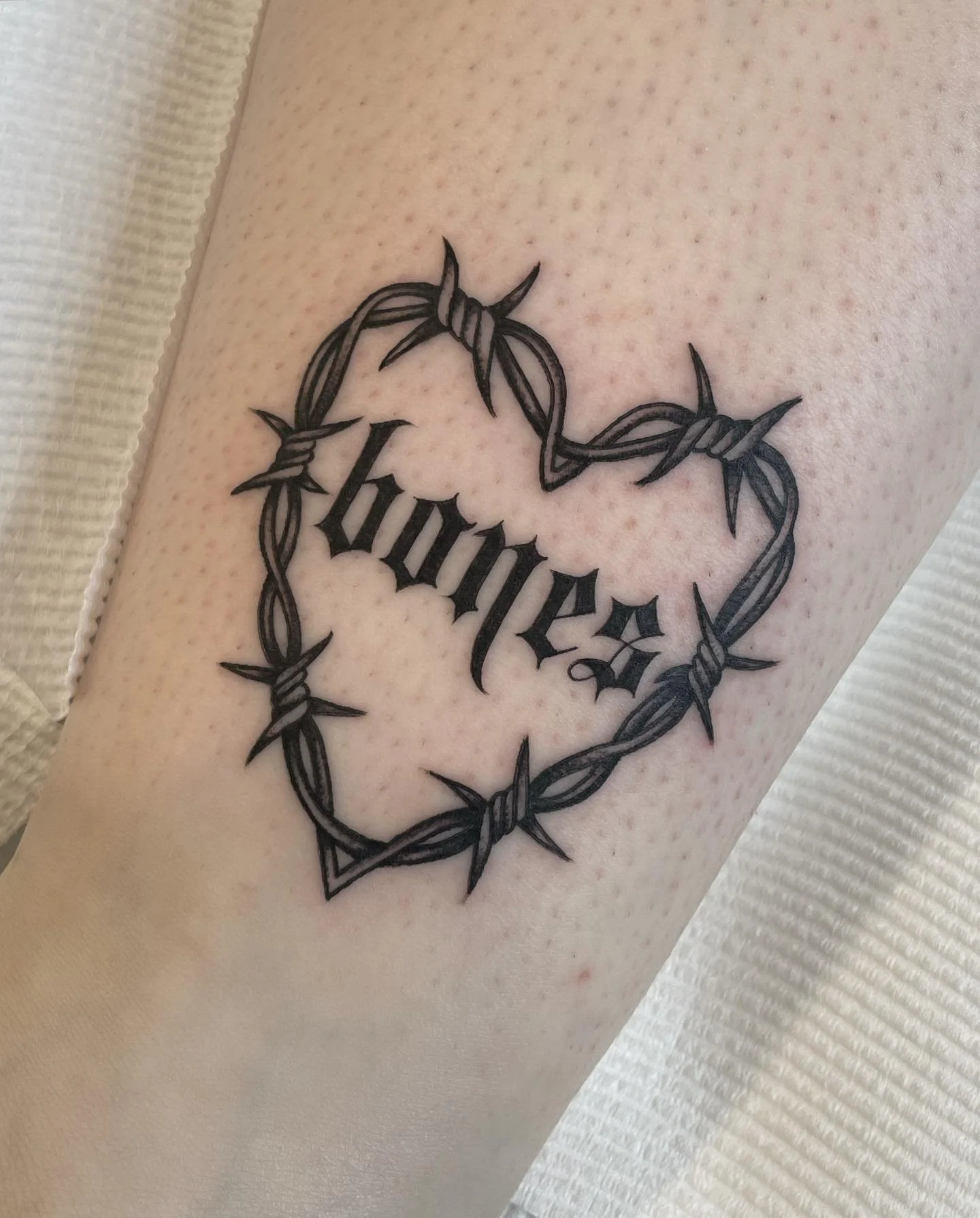 Tattoo of the word "Loyalty" in gothic script surrounded by a heart-shaped barbed wire design on the skin.