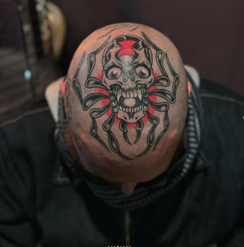 Tattoo of a skull with spider legs on the top of a person's shaved head.
