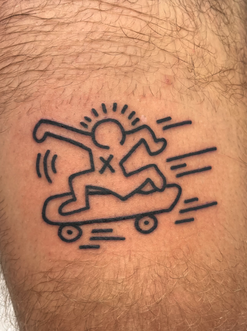 Tattoo of a stick figure riding a skateboard with a sun halo, lines indicating motion around the skateboard and figure's arms, and an X on the chest.