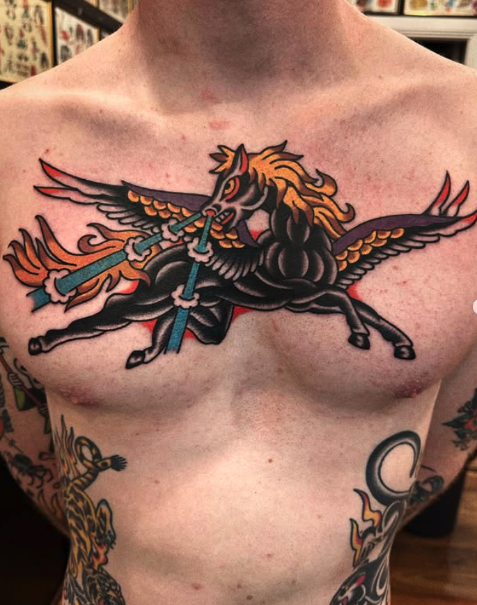 Tattoo of a mythical black Pegasus with a golden mane, wings, and tail, holding blue lightning bolts in its mouth, on a person's chest.