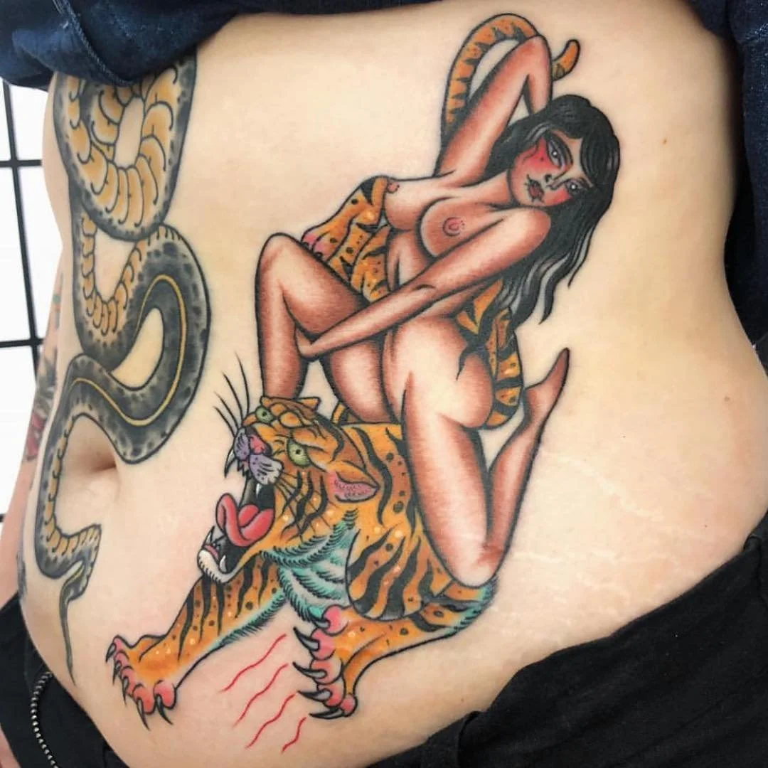 Tattoo of a woman with black hair posing with a tiger, with a snake wrapping around her body.