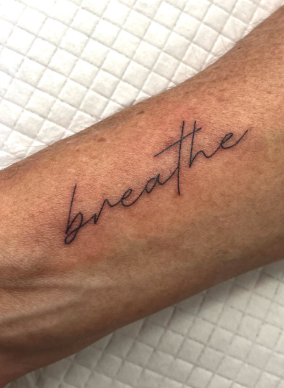 Tattoo of the word 'breathe' written in cursive on a person's inner forearm.