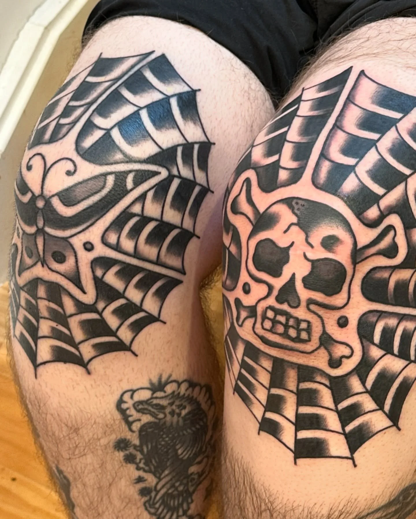 Tattoo of a skull with spiderwebs on the person's upper thighs, with a lion tattoo visible on the lower thigh.