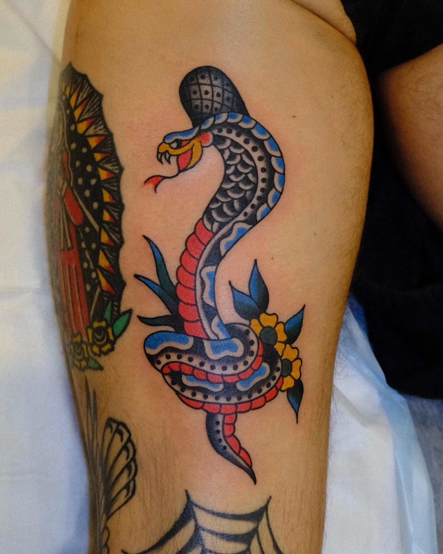 Colorful tattoo of a snake wrapped around a bouquet of flowers on a person's arm.