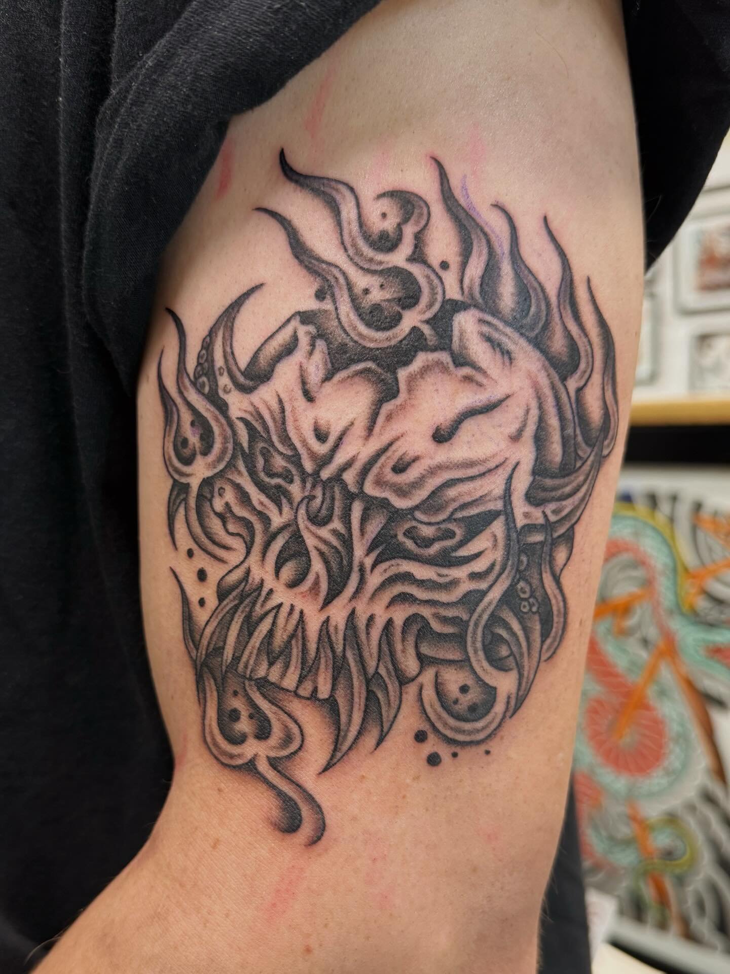 Tattoo of a stylized lion's face with flowing, flame-like mane on person's upper arm.