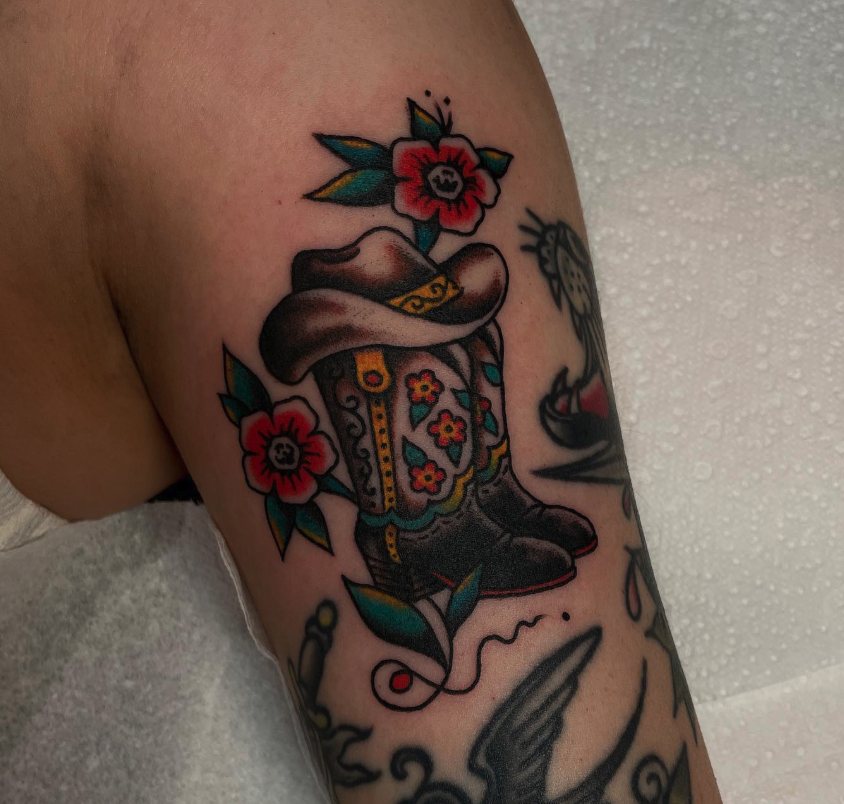 Colorful tattoo of a gnome with a beard, wearing a hat, surrounded by red flowers and green leaves.