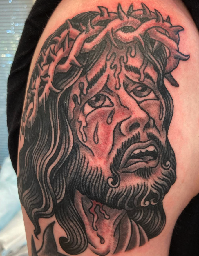 Tattoo of Jesus Christ with a crown of thorns, tears on his face, and a sorrowful expression.