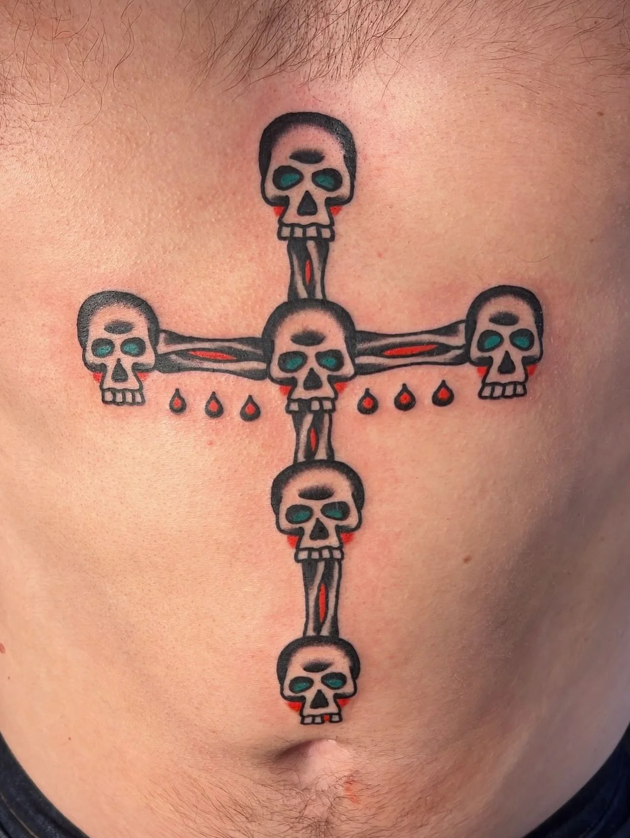 Tattoo of a cross made of skulls with dripping red droplets on skin.