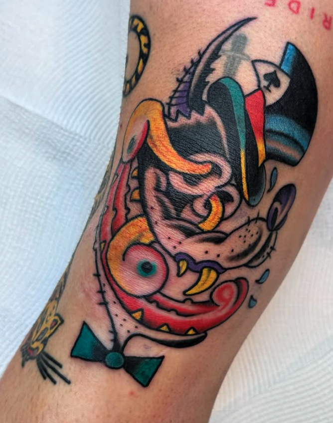 A colorful tattoo on a person's arm featuring abstract and cartoonish elements, including a face with exaggerated features, bright colors, and clothing accessories.