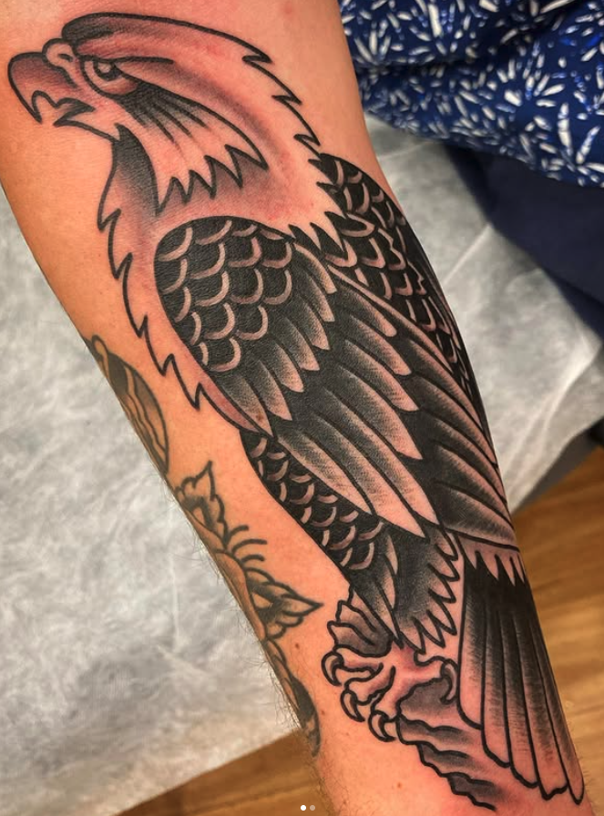 Black and gray tattoo of an eagle on person's forearm, featuring detailed feathers and an open beak.
