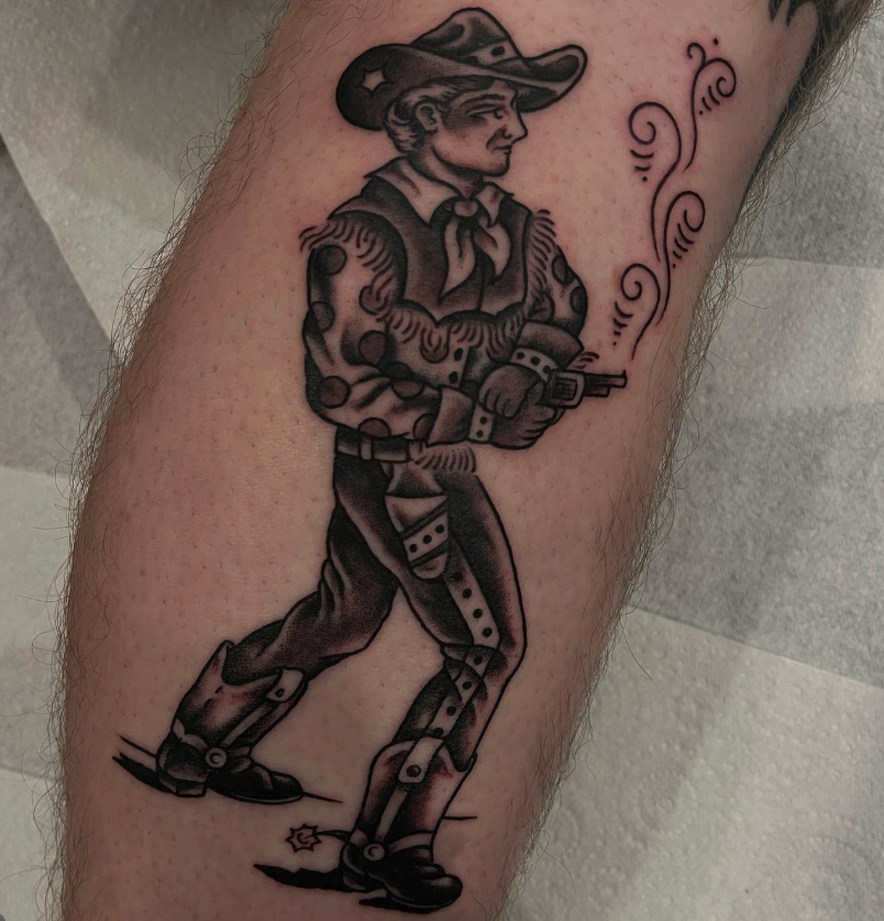 Black and gray tattoo of a cowboy with a hat, bandana, and polka-dot shirt, holding a gun with smoke rising from it, on a person's leg.