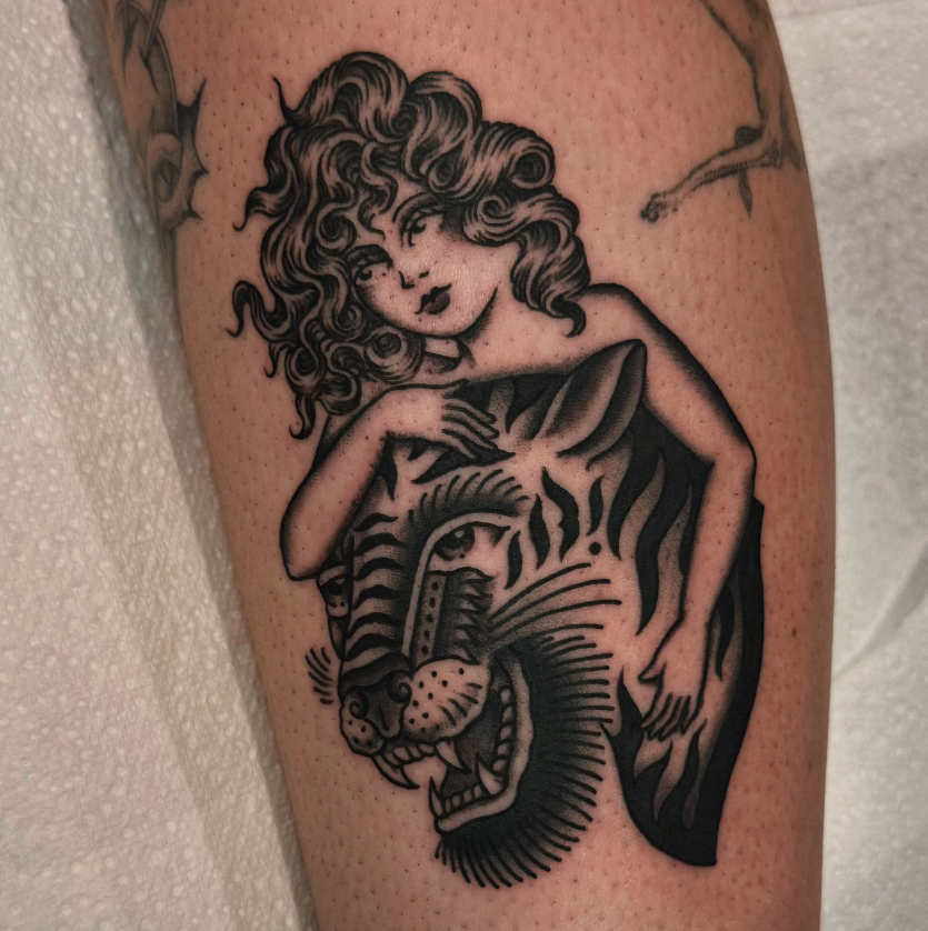 Tattoo of a woman with curly hair resting her head on a tiger's head. The tiger is stylized with bold black lines and detailed features.