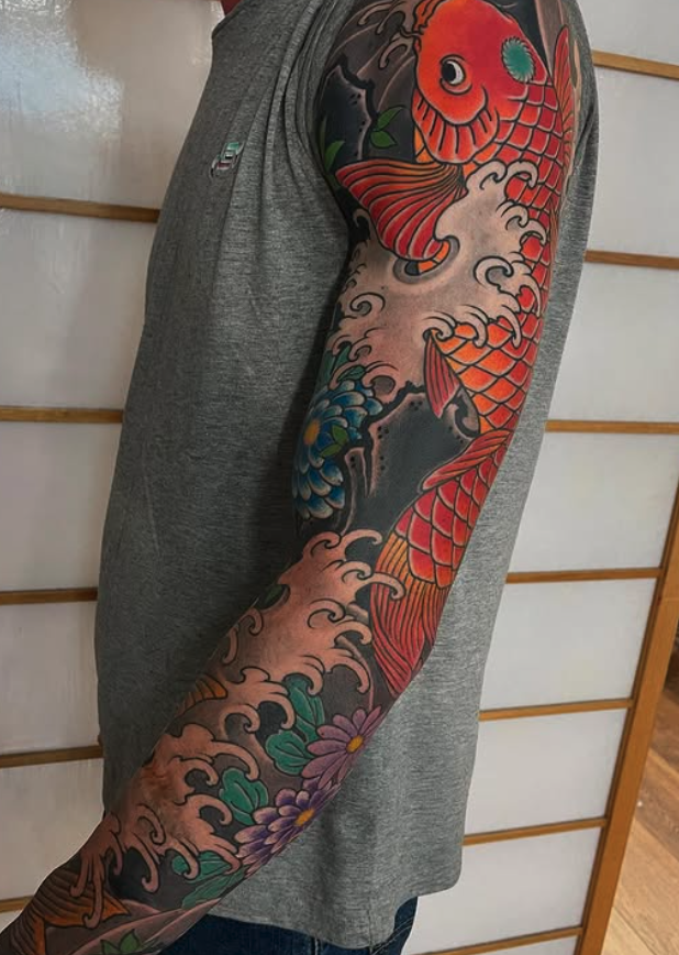 A person with a colorful Japanese-style koi fish tattoo on their arm, featuring waves and flowers.