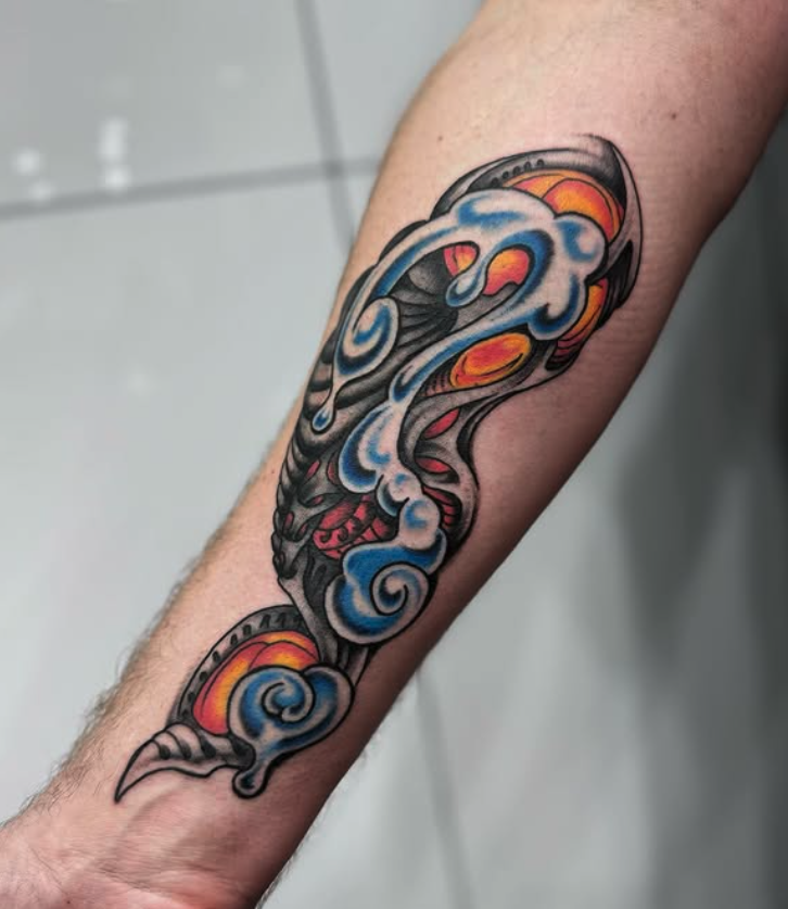 Colorful tattoo of a stylized whale emitting water, with orange and yellow sun-like elements and blue swirling clouds or waves.