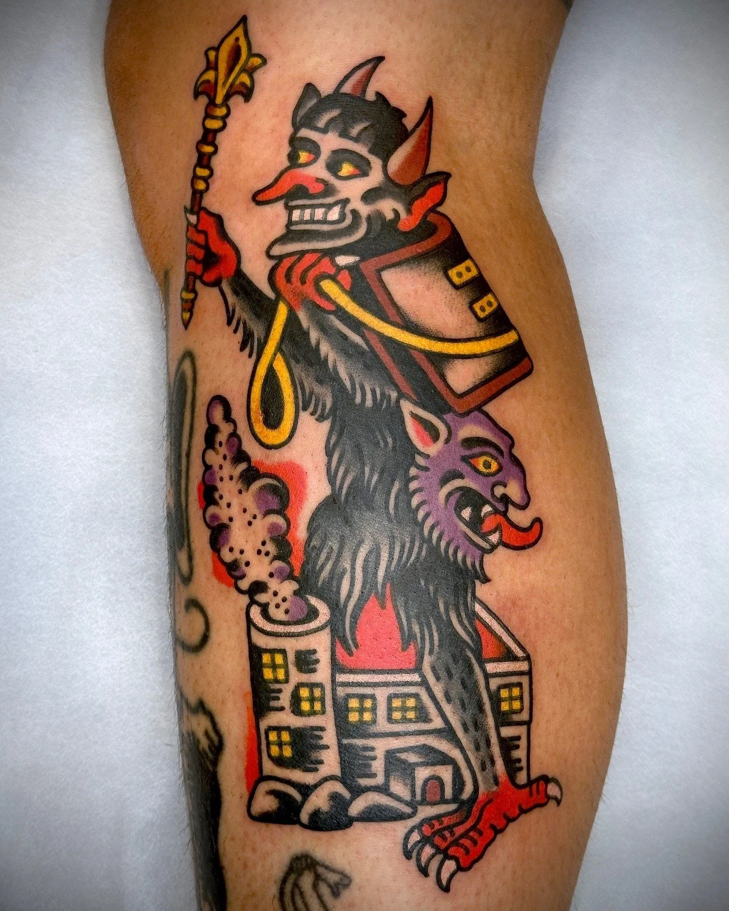 Tattoo of a cartoonish devil and lion figure standing on a factory with smoke coming out of its chimney.
