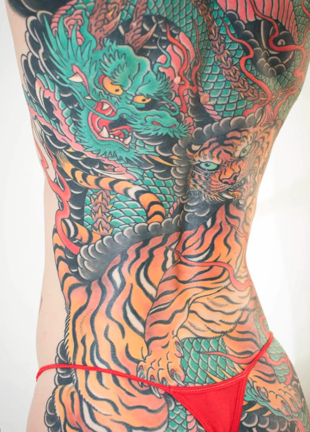Colorful tattoo of a fierce dragon and a tiger on a person's torso, with vibrant scales and stripes.