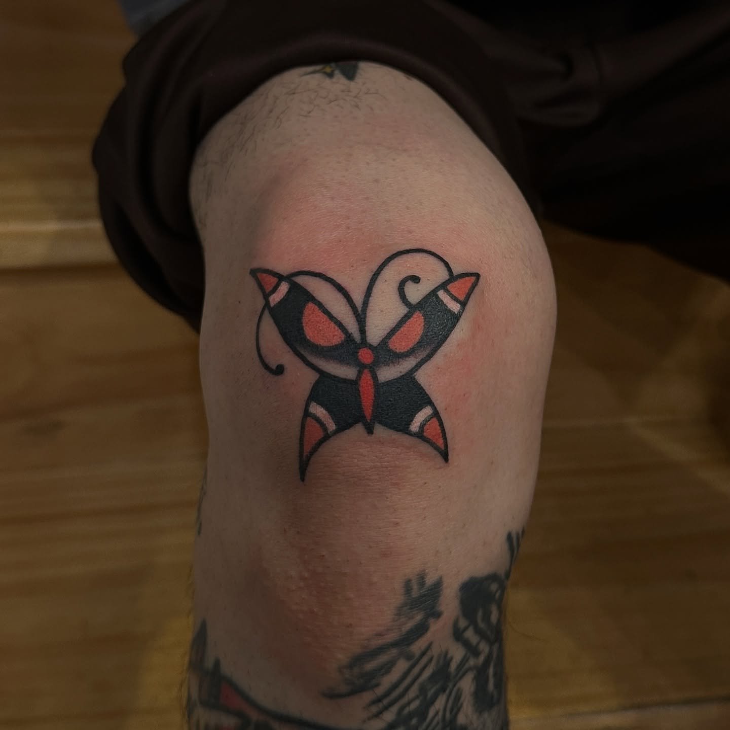 Tattoo of a stylized butterfly on a person's upper arm with black, red, and orange colors.