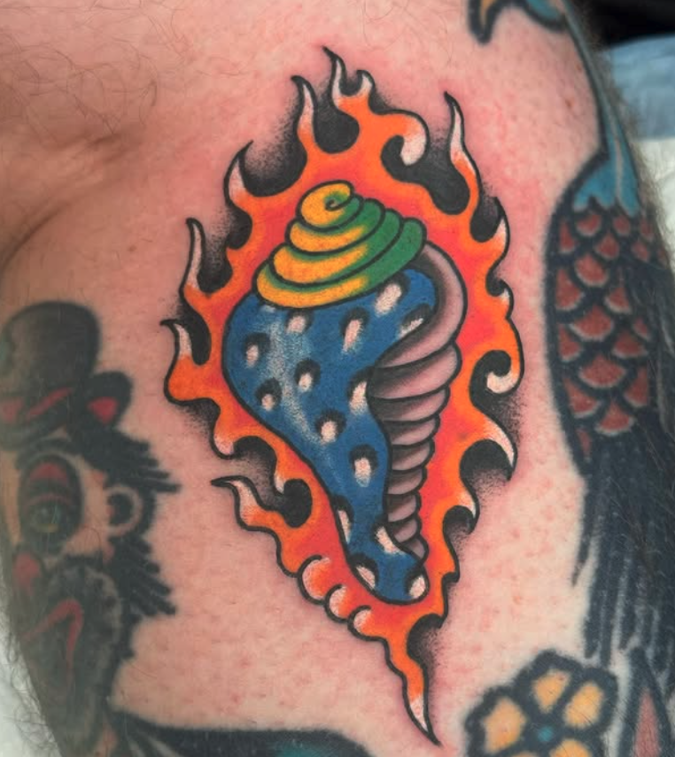 Colorful tattoo of a stylized, snake-like creature with a conical, yellow-green top, blue body with white spots, and a spiraled pink tail, surrounded by flames in orange and black.