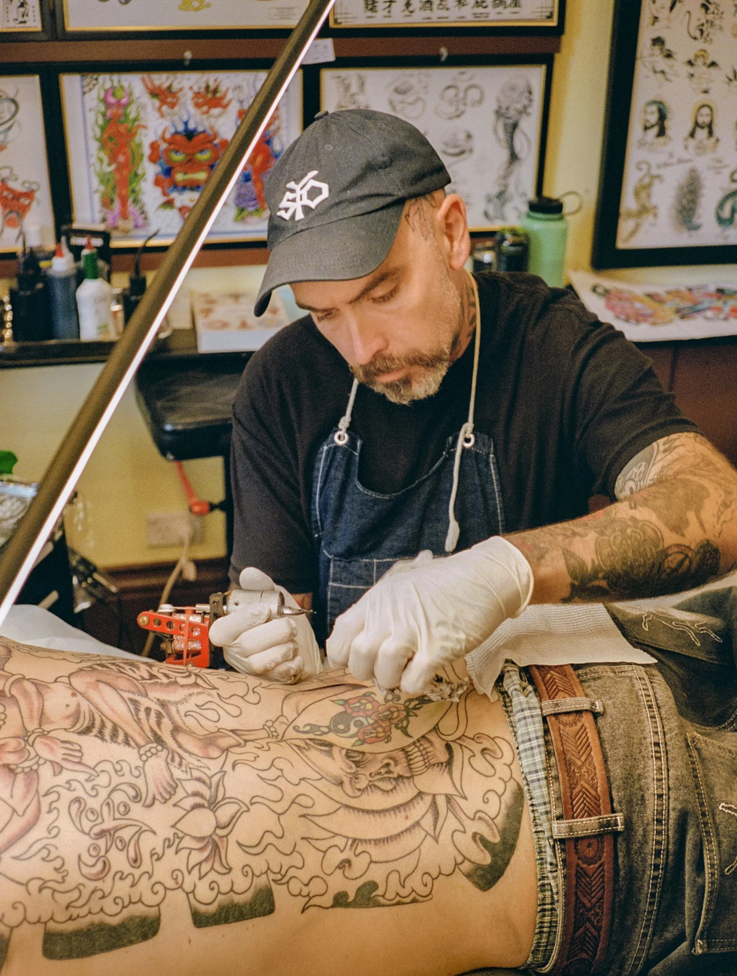 Tattoo artist working on a large tattoo on a person's arm in a tattoo studio.