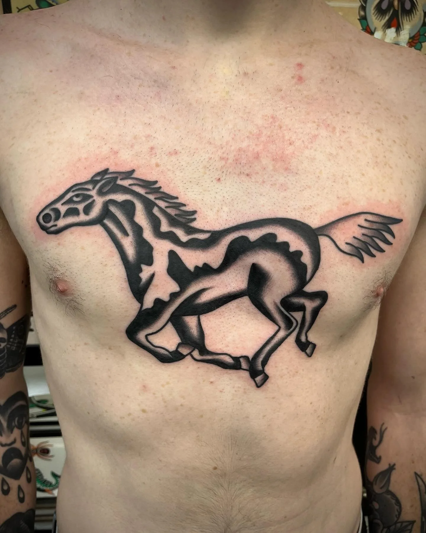 Tattoo of a stylized running horse with bold black outlines on a person's chest.