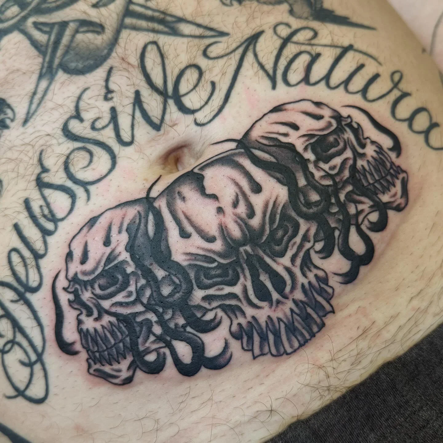 Tattoo of a skull with snake-like elements and a phrase in cursive above it on human skin.